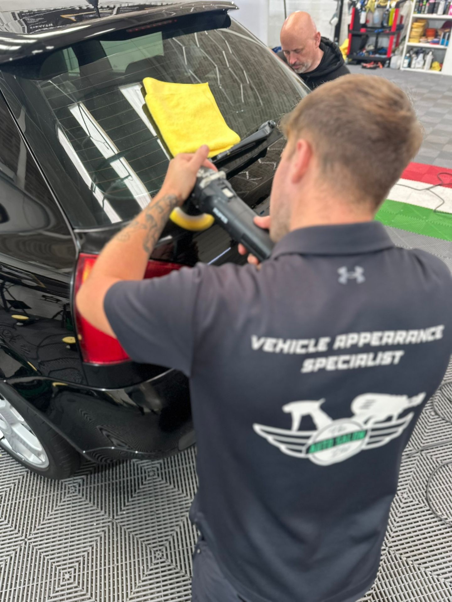 Vehicle appearance specialist polishing the rear window of a black car with a cloth placed on top.