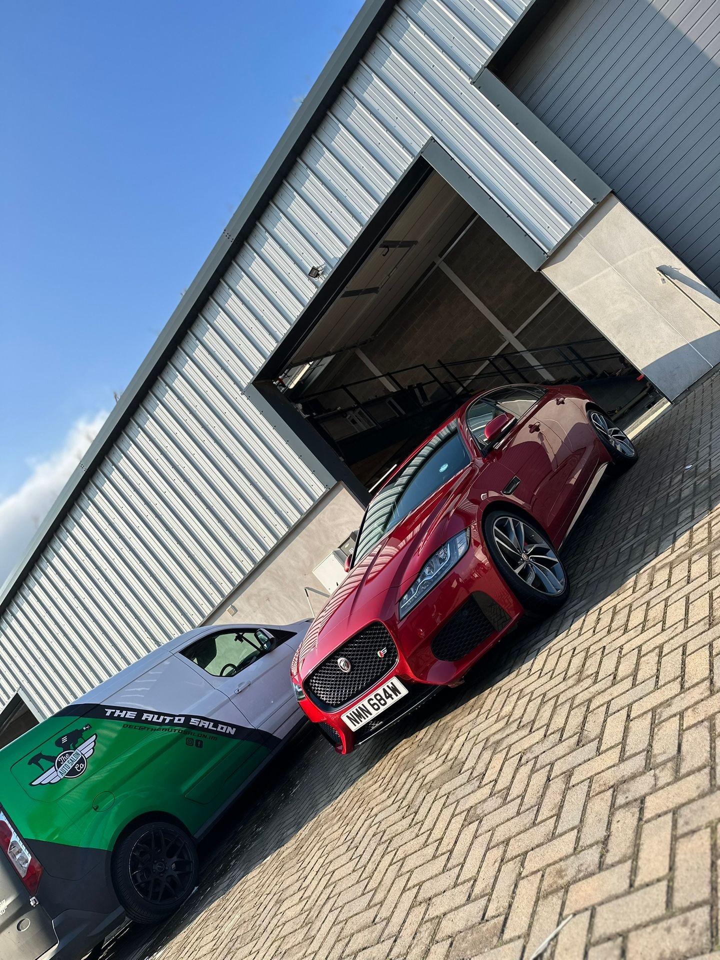 Red sports car and green van parked outside a gray metal garage.
